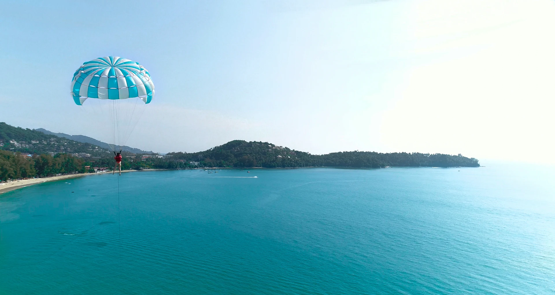 A person parasailing over Bang Tao Bay against a backdrop of tropical hills