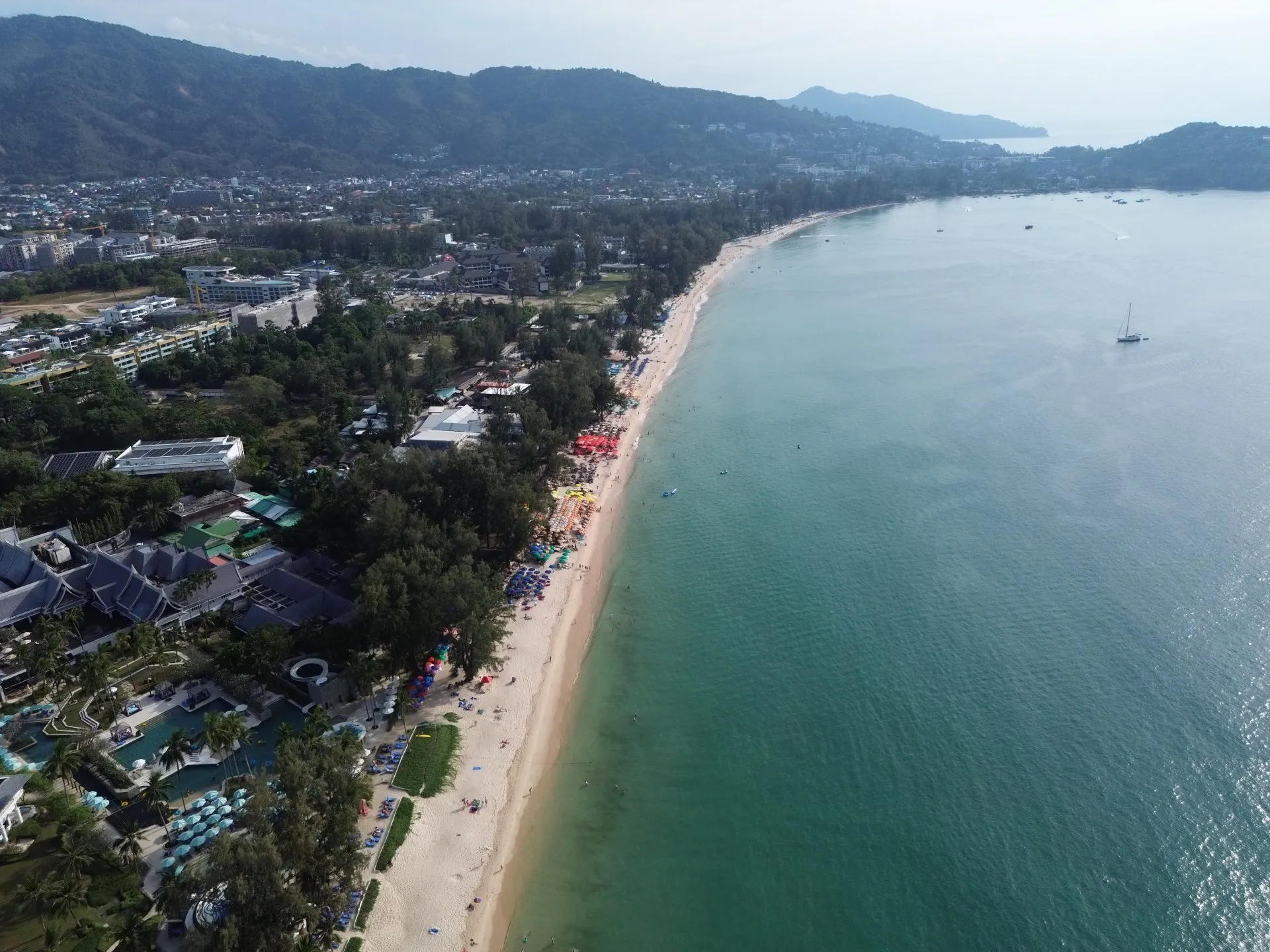 Panoramic view of Bang Tao Bay from above: blue sky, turquoise water, and a long sandspit