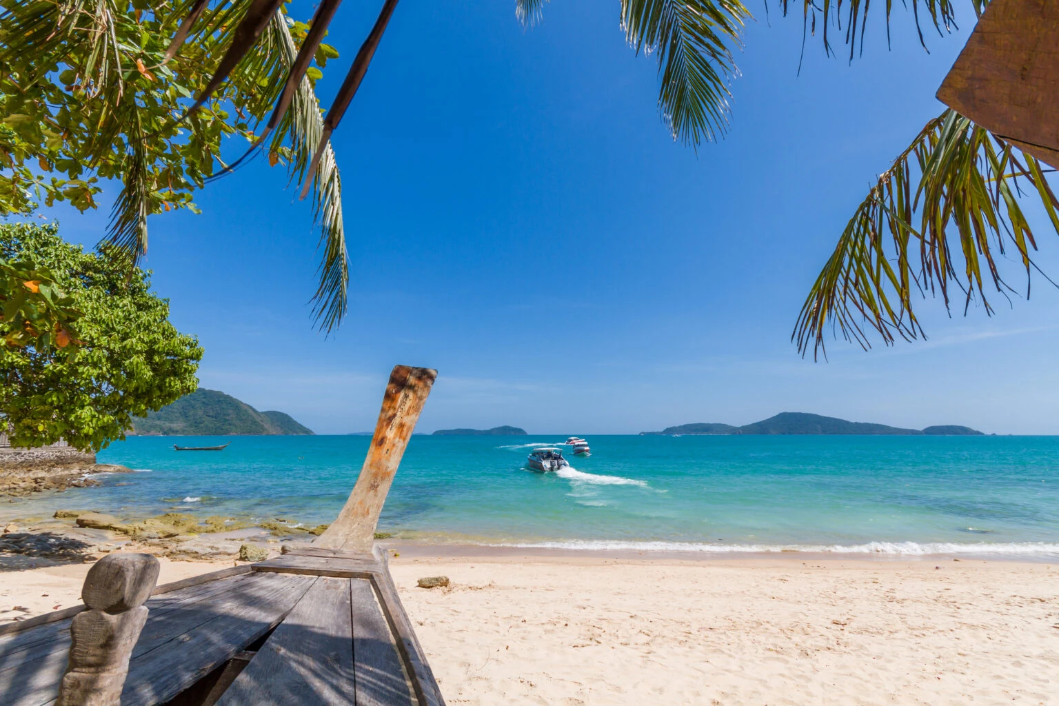 View of the tropical Bang Tao beach in Phuket with a wooden boat in the foreground and speedboats in the sea