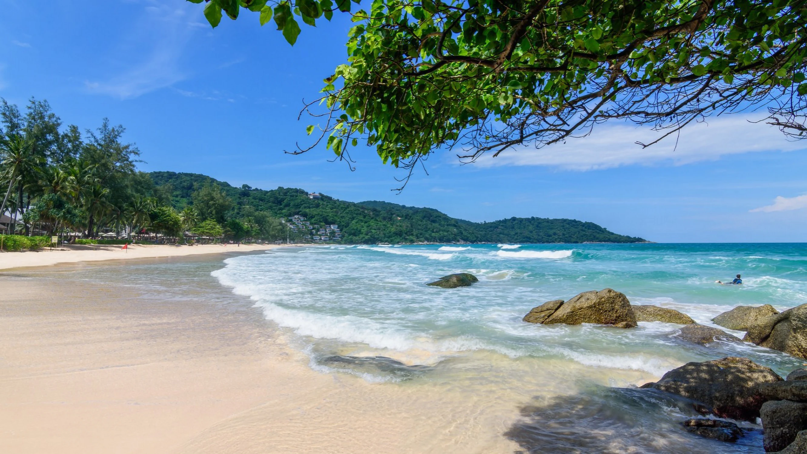 Karon sandy beach in Phuket with turquoise water and green hills in the background
