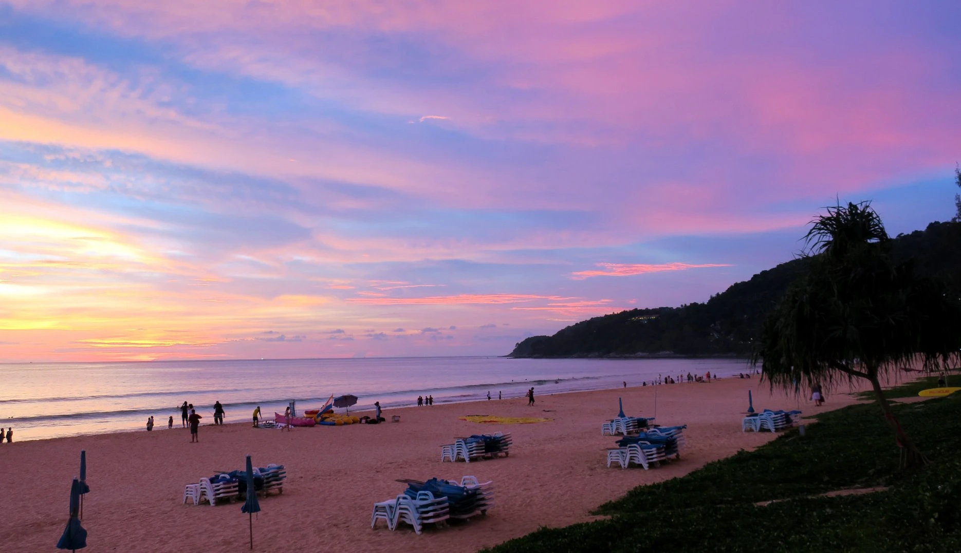 Sunset at Karon Beach: pink and purple sky over the ocean and silhouettes of vacationers on the sand