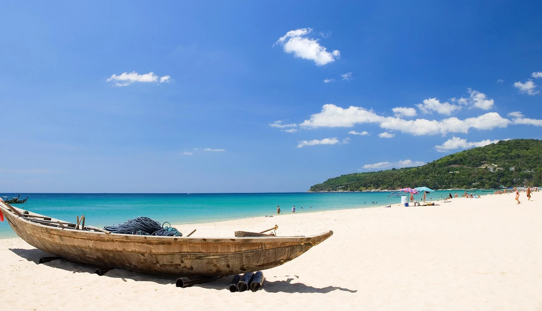 Wooden boat on the white sand of Karon beach under a clear blue sky