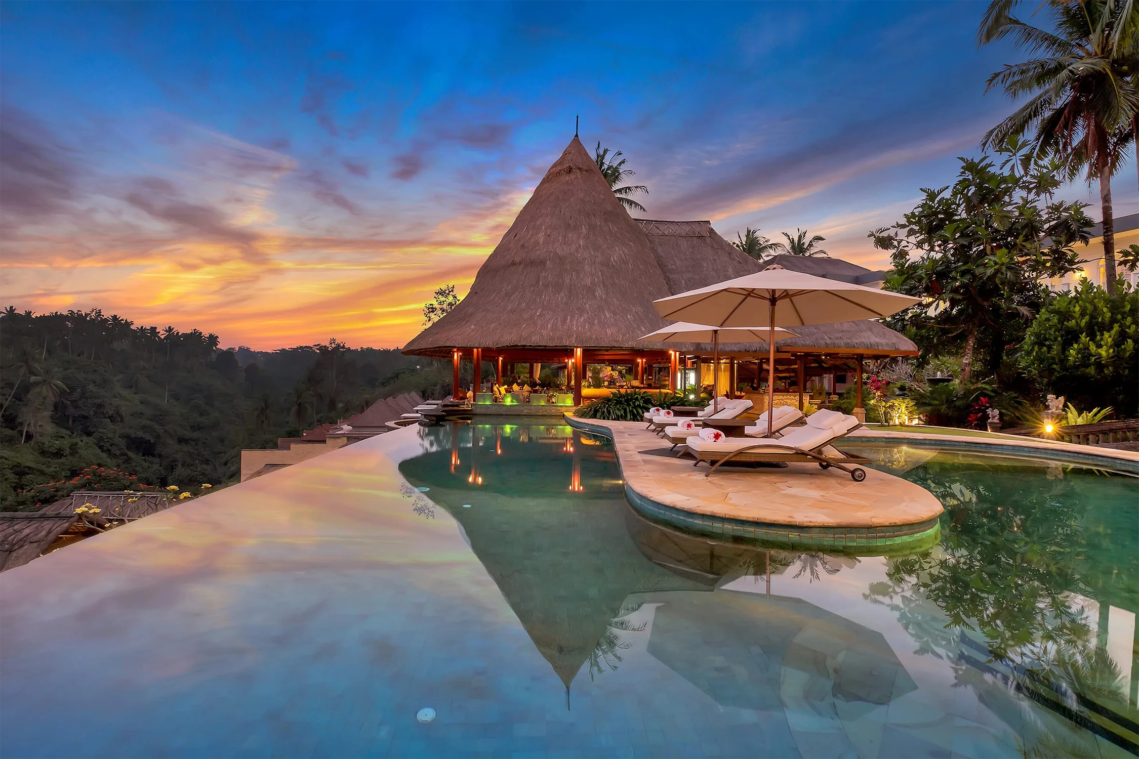 Infinity pool and thatched bungalow in Bali against a tropical jungle sunset
