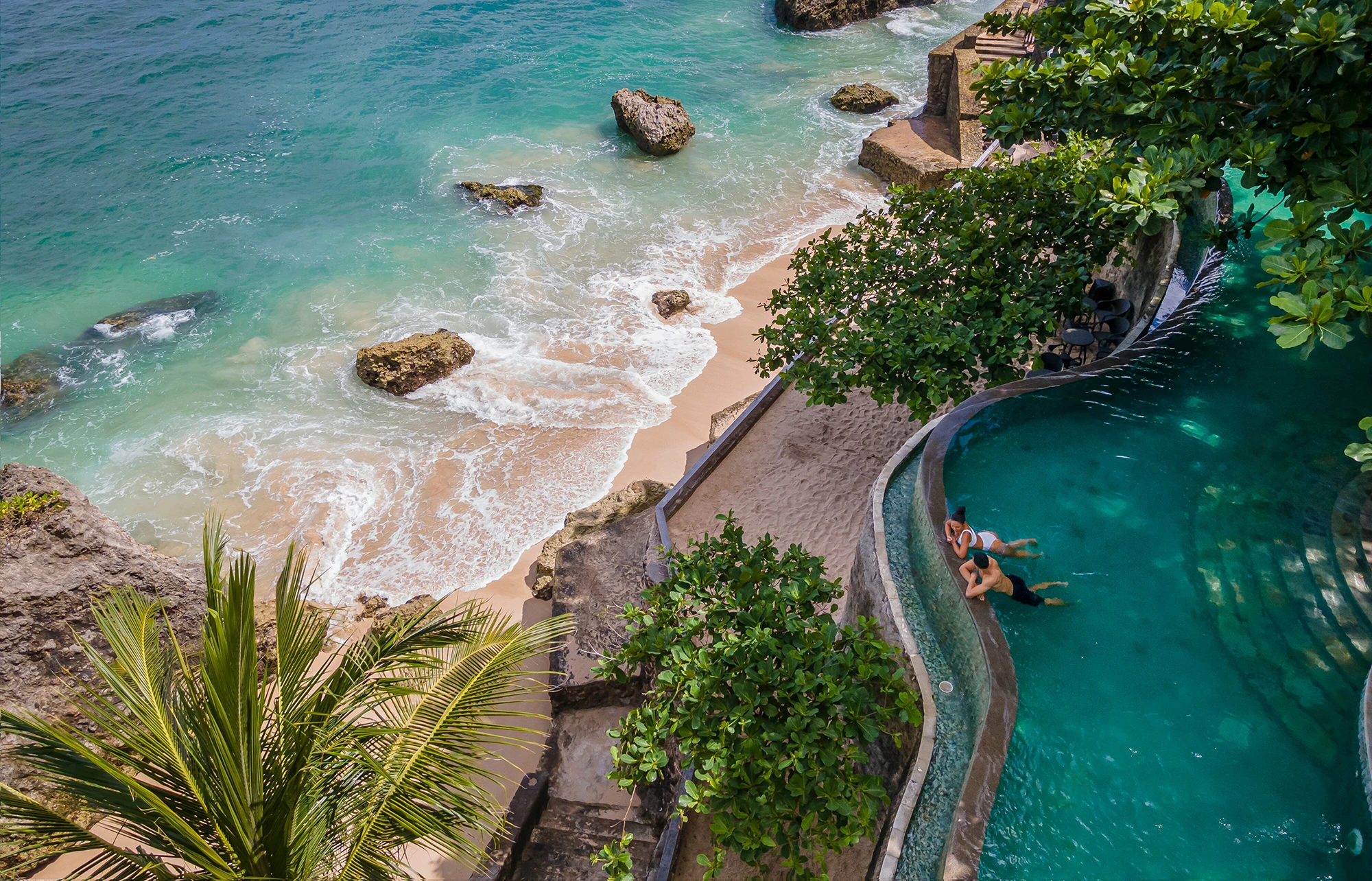 A cliffside pool by the ocean in Bali overlooking a sandy beach and the surf